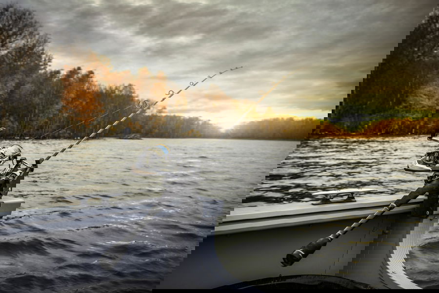 Beginner fishing combo with spinning reel mounted on a boat over calm lake water at sunset.