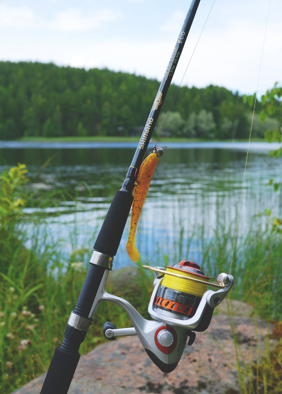 Fishing rod with a yellow lure and spinning reel by a serene lake.