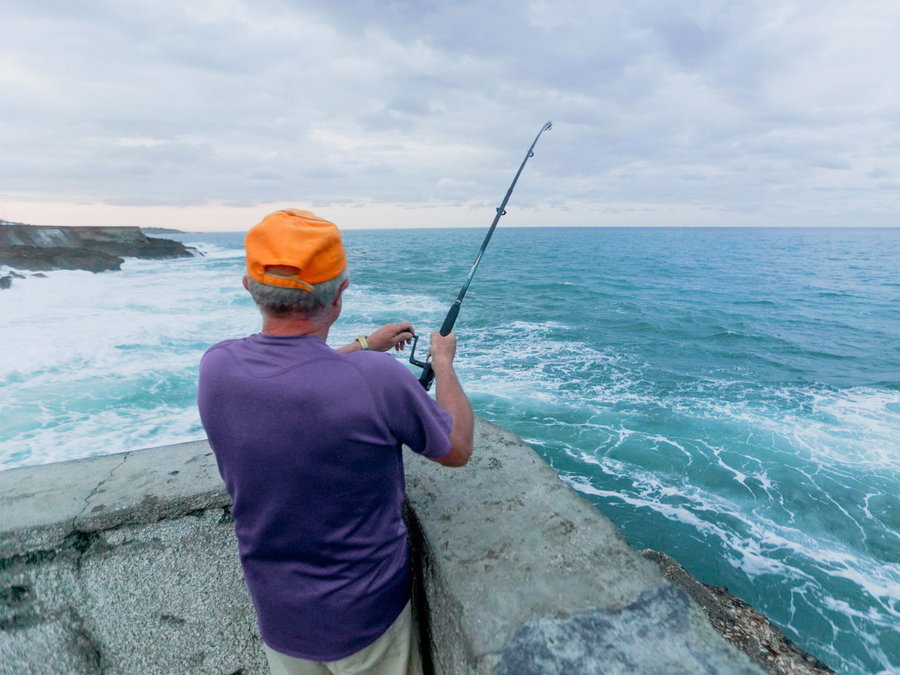 A person fishing from a rocky shore overlooking the ocean waves.