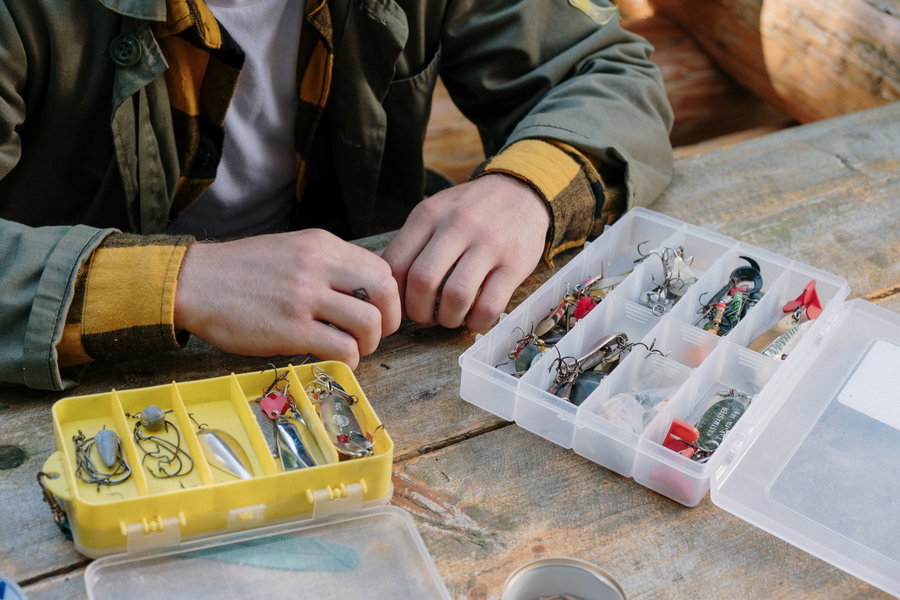 Hands organizing fishing hooks and lures in tackle boxes on a wooden table.