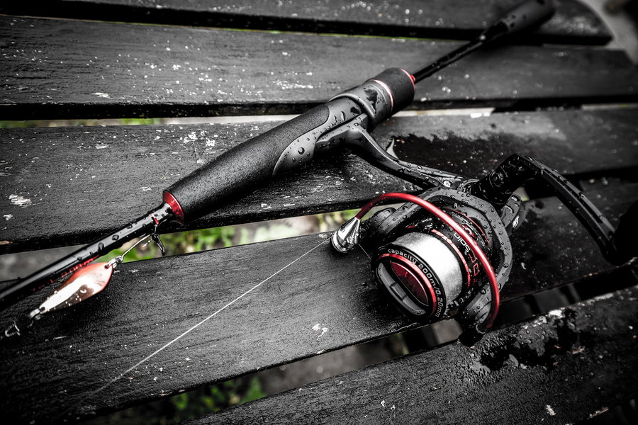 Trout fishing rod and reel resting on a wet wooden surface.
