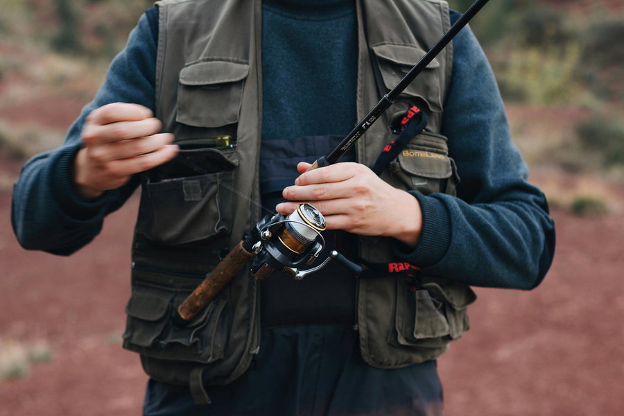 Angler adjusting fishing line on a rod while wearing a fishing vest.