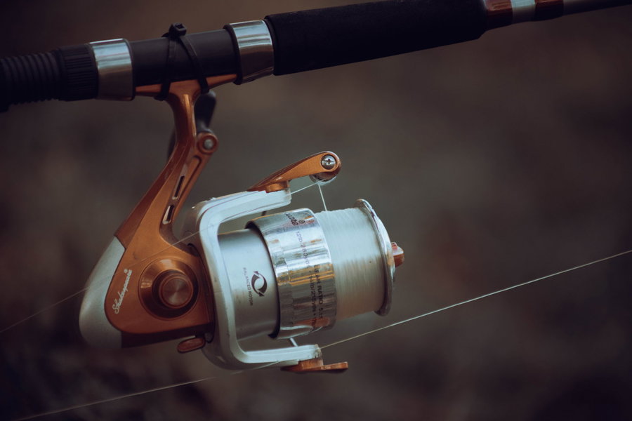 Spinning reel with silver spool and orange accents on a fishing rod.