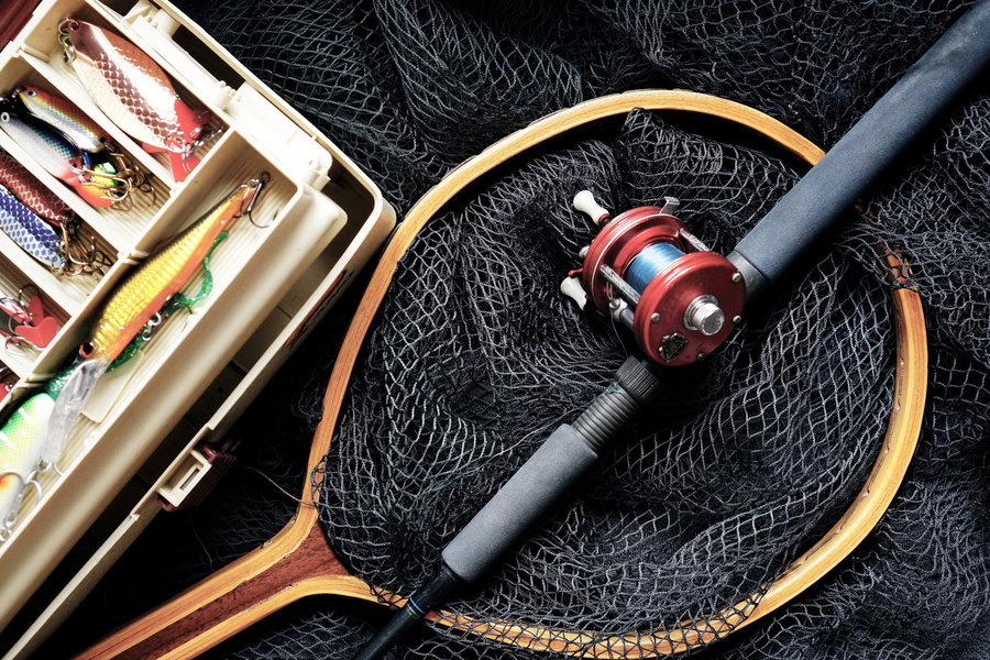 Fishing gear including lures, a fishing reel, and a net on a dark background.