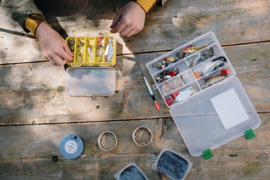Hands organizing fishing lures in tackle boxes on a wooden surface.