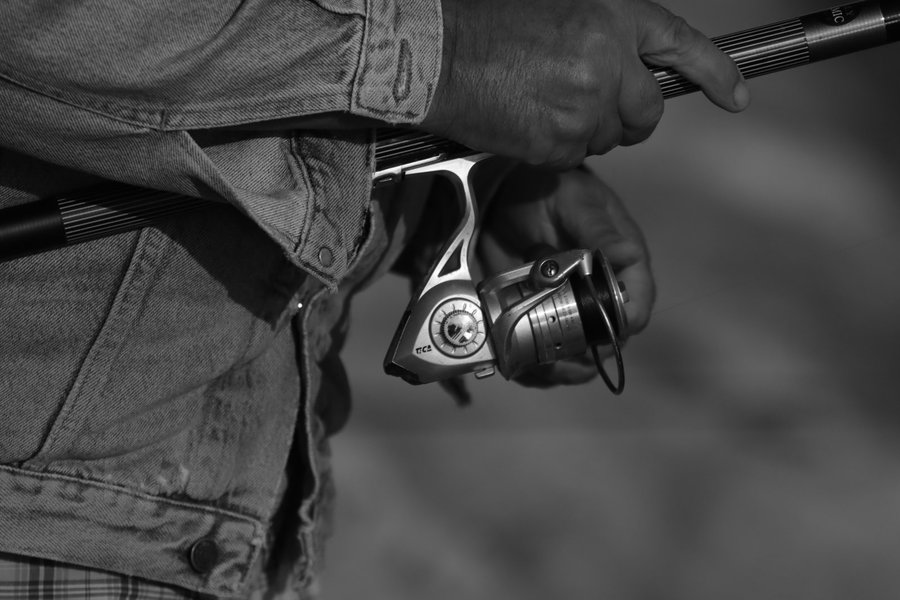 Hand holding a spinning reel attached to a fishing rod.