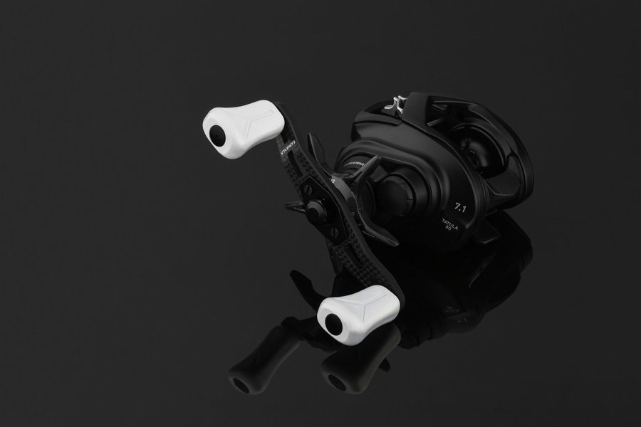 Baitcasting reel with white handles on a reflective black surface.
