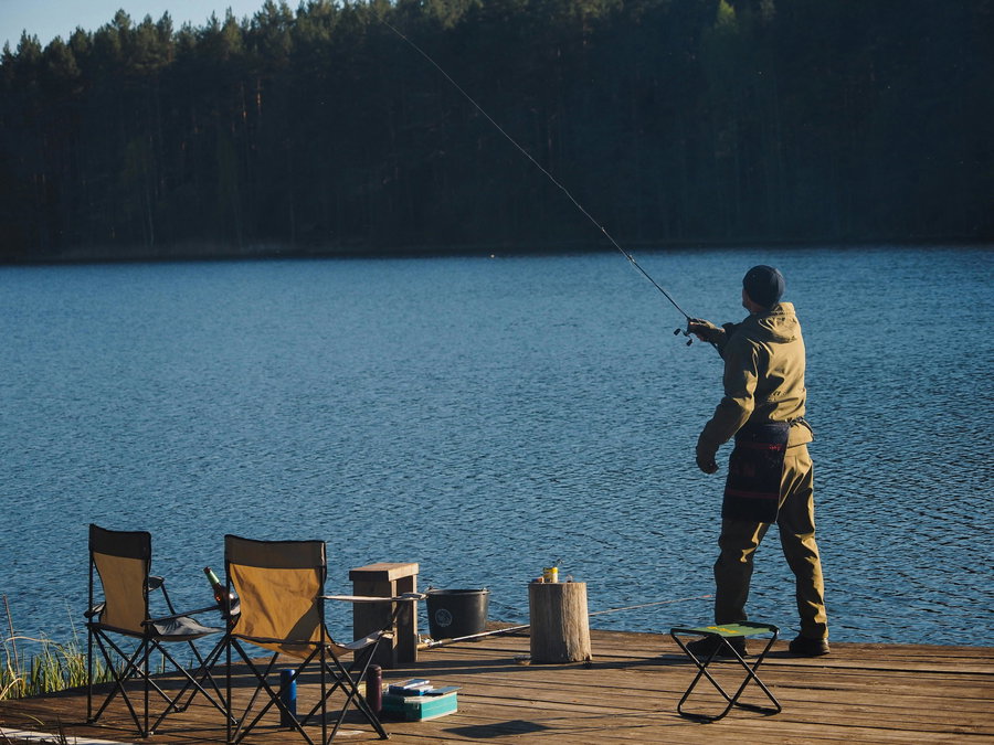 Fisherman casting a line from a wooden dock by a lake.