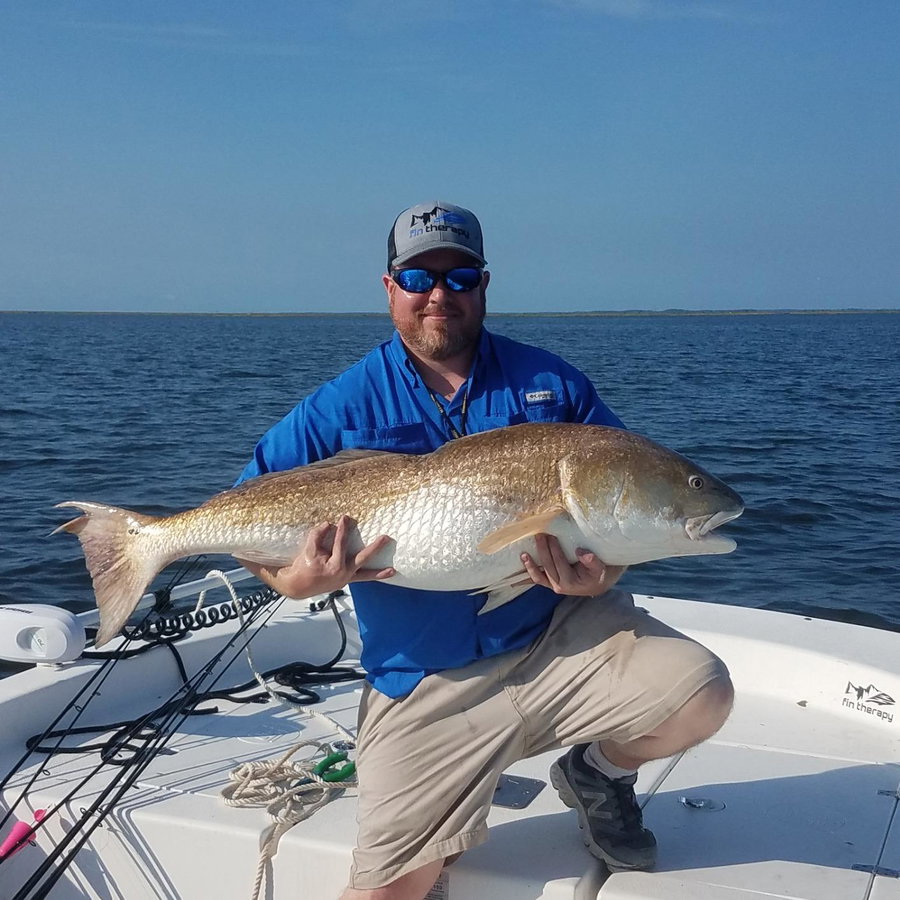 Angler proudly holds a large fish on a boat in open water.