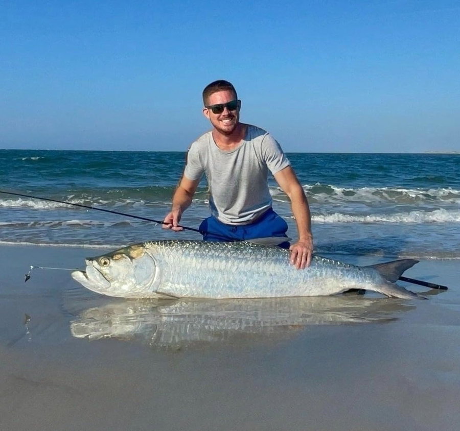 Smiling angler poses with a large fish on the beach.