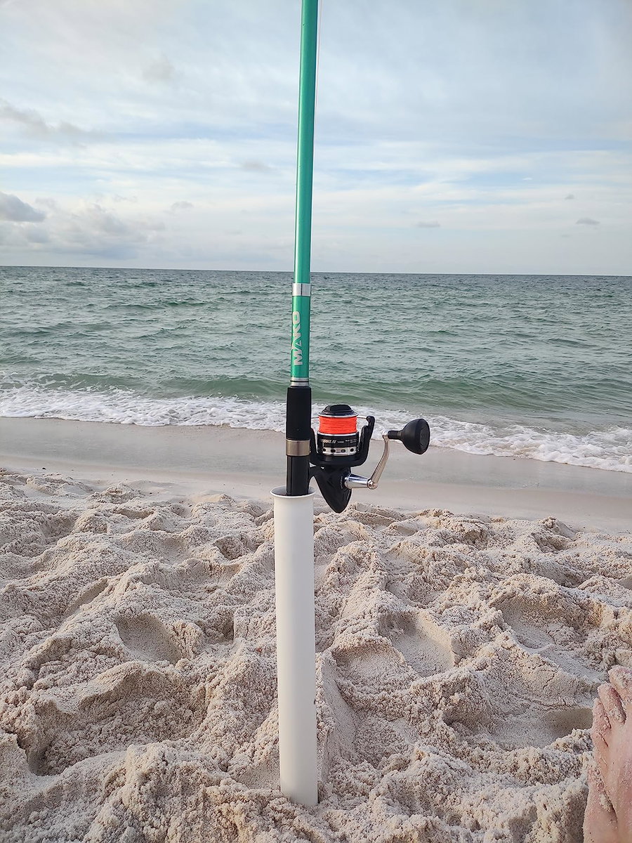 Fishing rod and reel set up on sandy beach by the ocean.