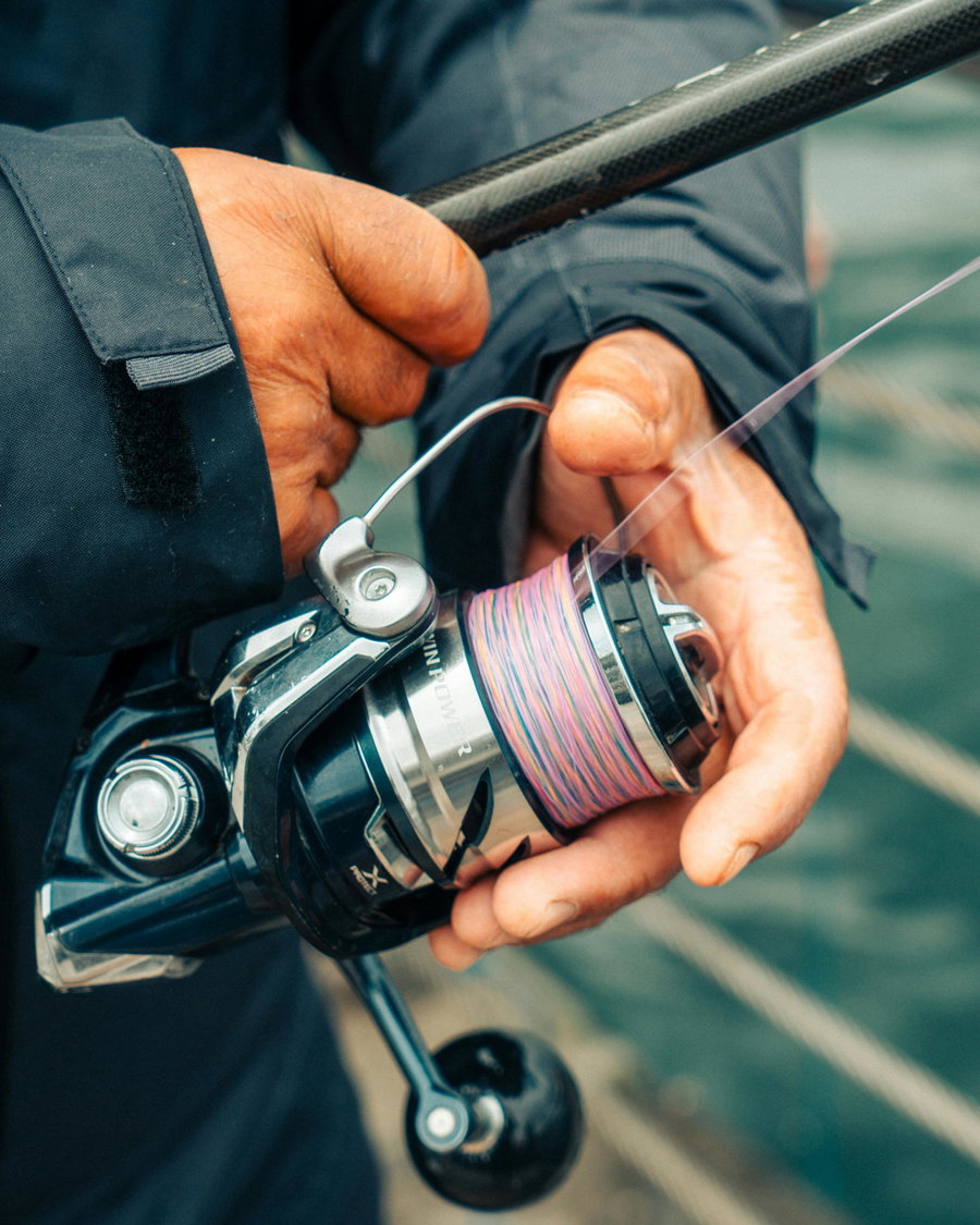 A person holding a spinning reel with colorful fishing line.