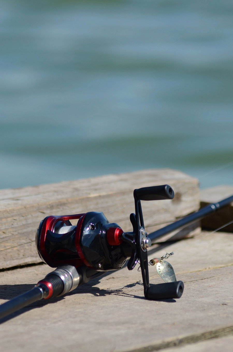 Fishing rod and reel resting on a wooden surface by the water.