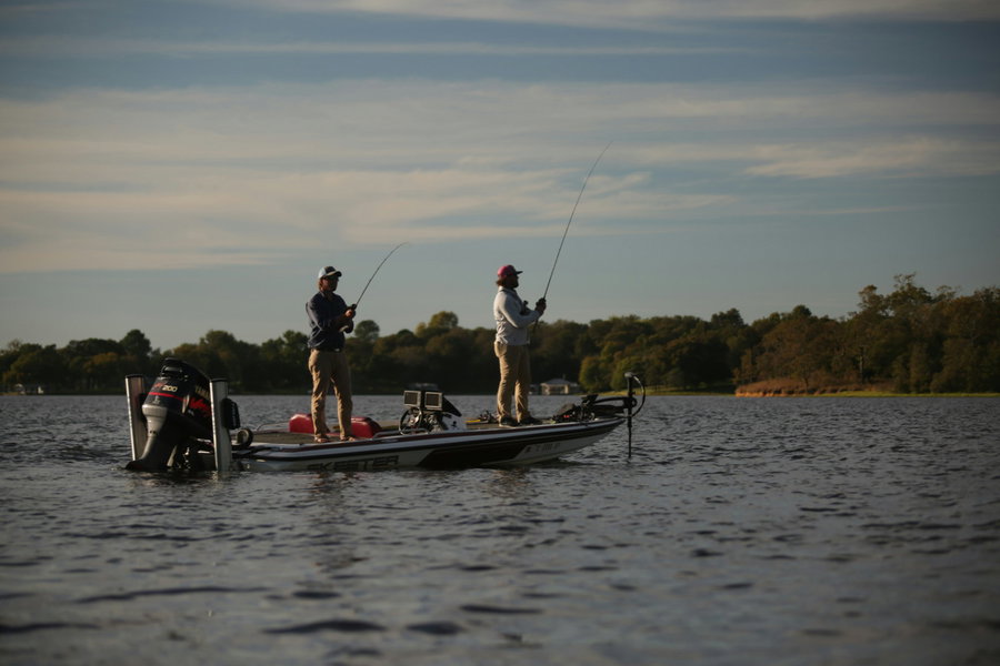 Two anglers fishing from a boat on a calm lake.