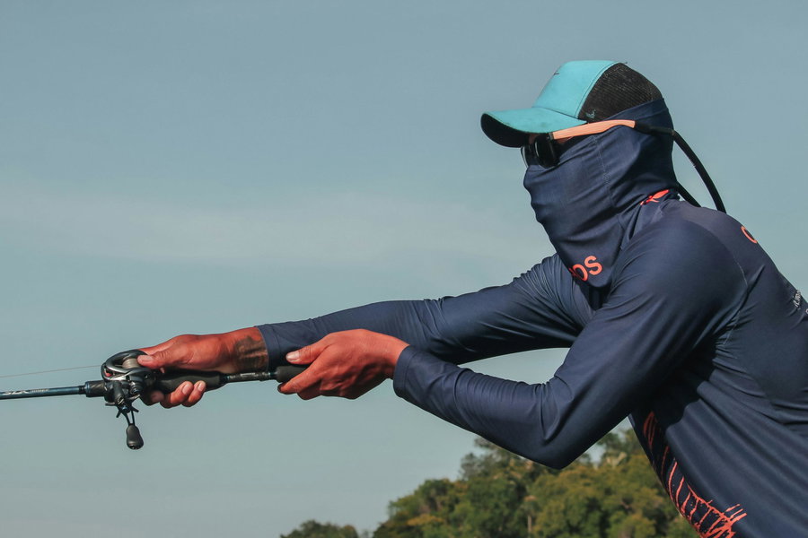 Fisherman casting a fishing rod with a baitcasting reel outdoors.