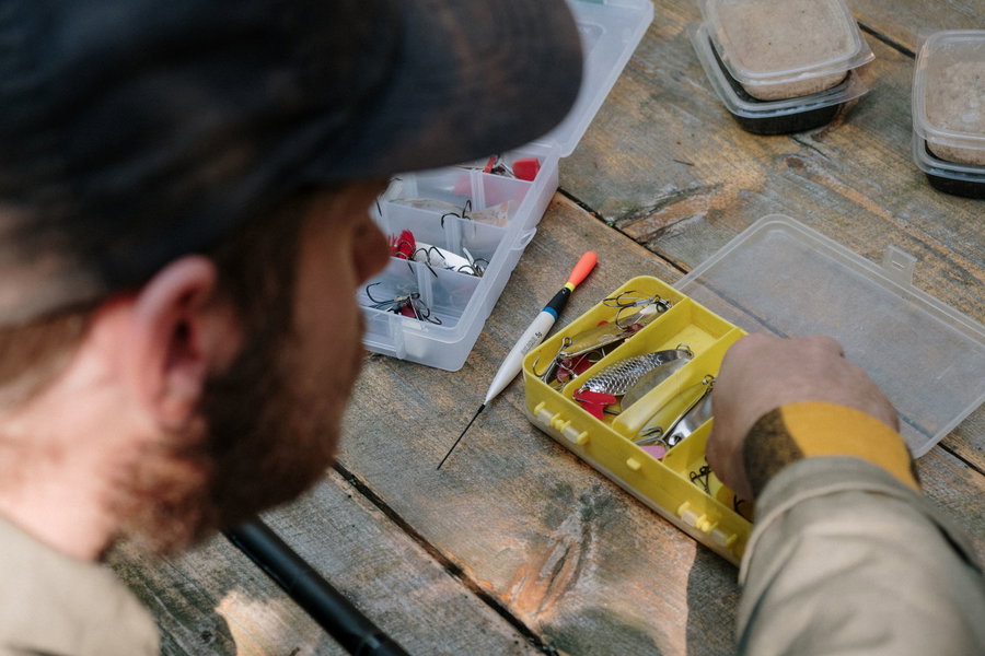 A person organizing fishing tackle in a yellow box on a wooden table.