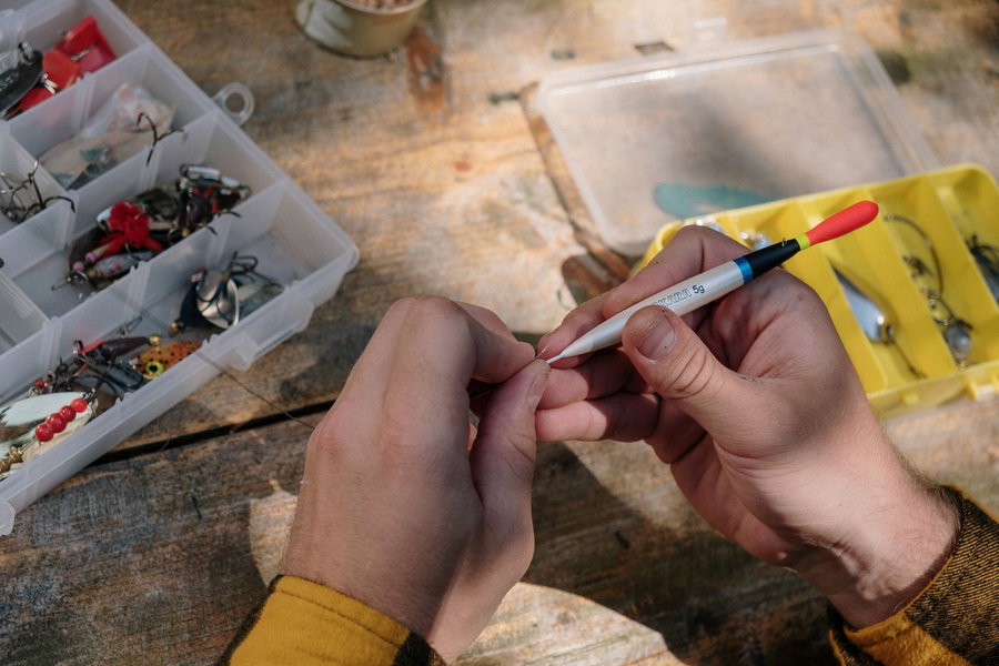 Hands tying fishing line with tools and tackle box in the background.