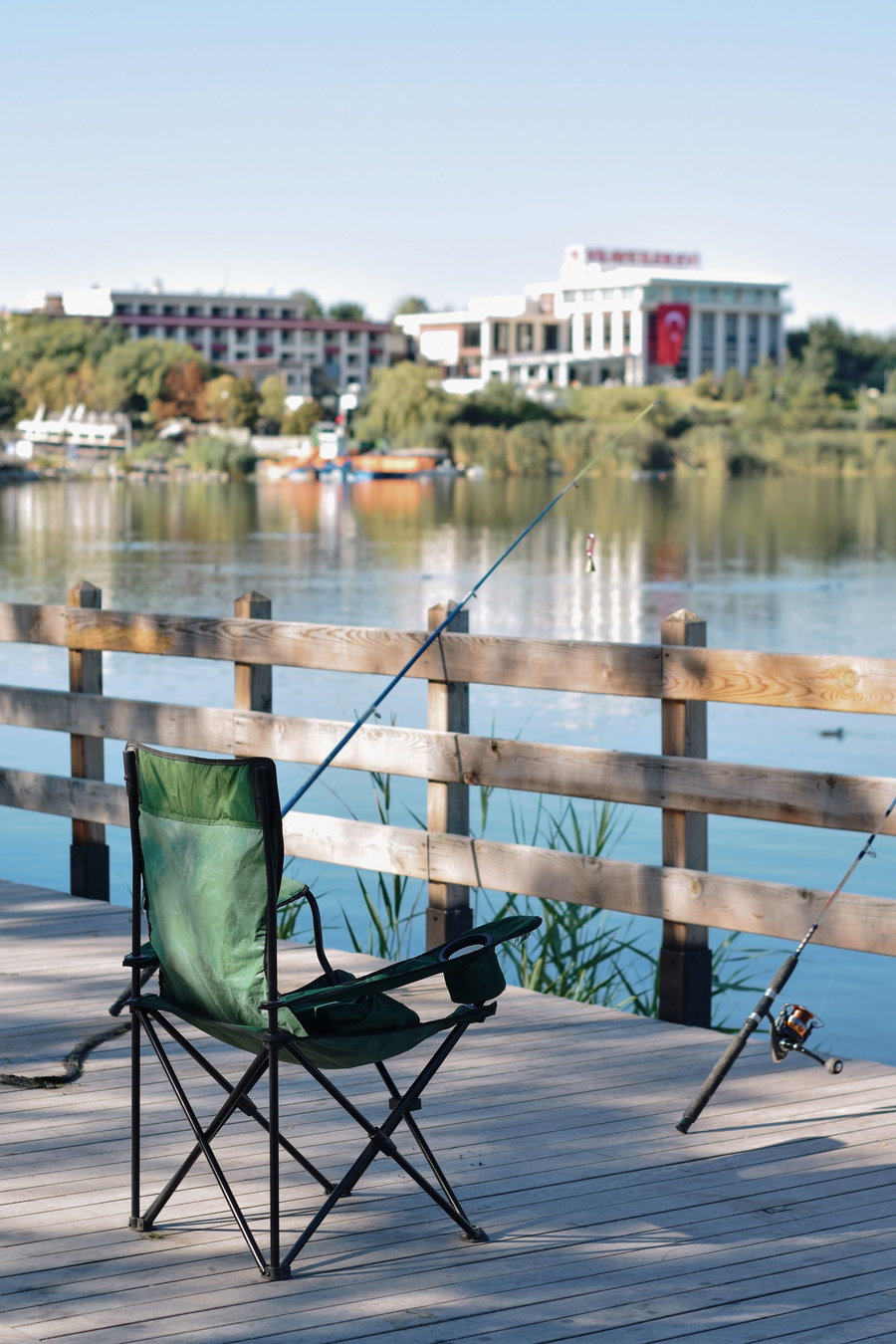 Green fishing chair beside a calm lake with fishing rods.