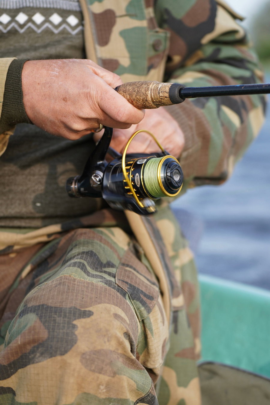 A person holding a fishing rod with a spinning reel, wearing camouflage clothing.