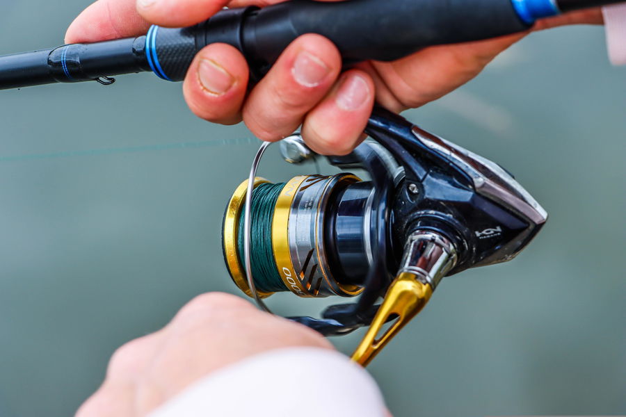Close-up of a spinning fishing reel and rod showing line setup and grip detail.