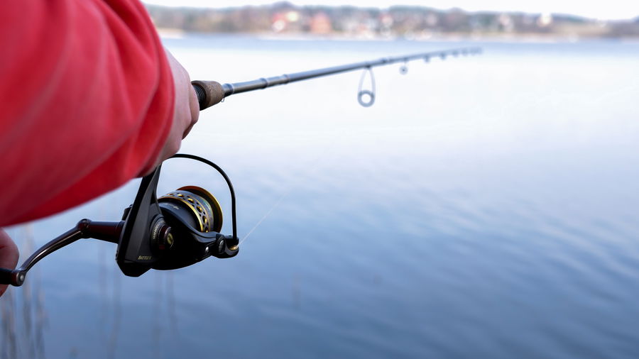 Close-up of a beginner casting a spinning fishing rod over calm water, showing proper grip and rod position.