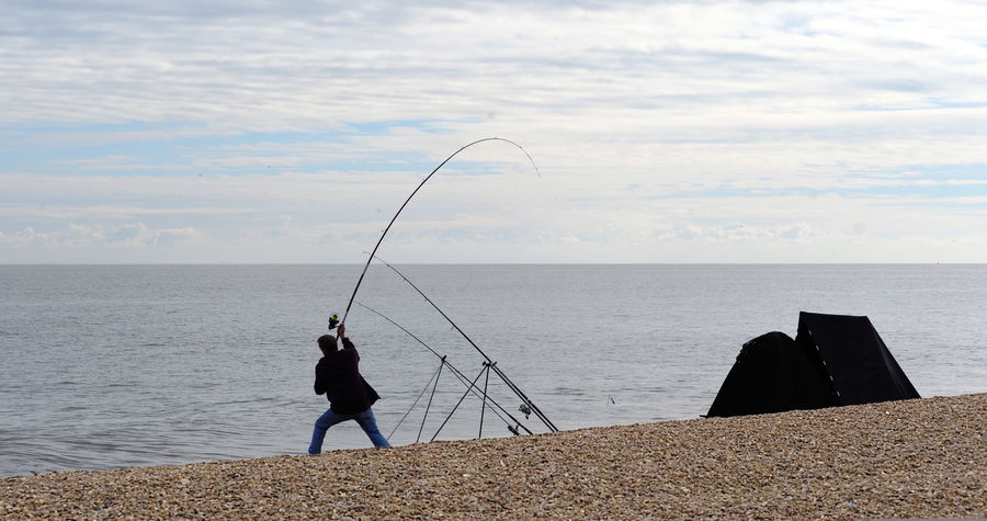 Angler fighting a strong fish from the shore with a deeply bent fishing rod under tension.