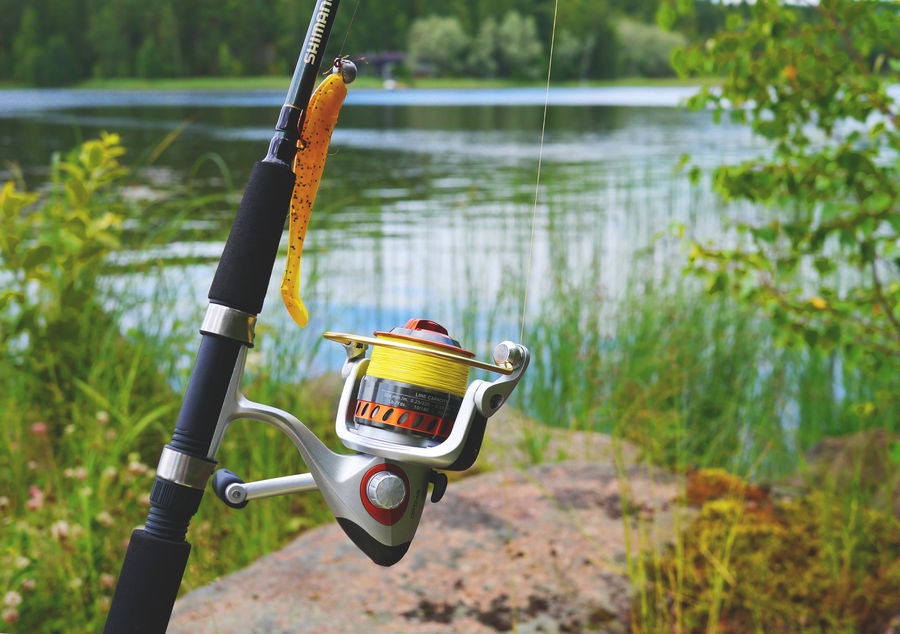 Spinning fishing reel spooled with fresh yellow line near a calm lake.