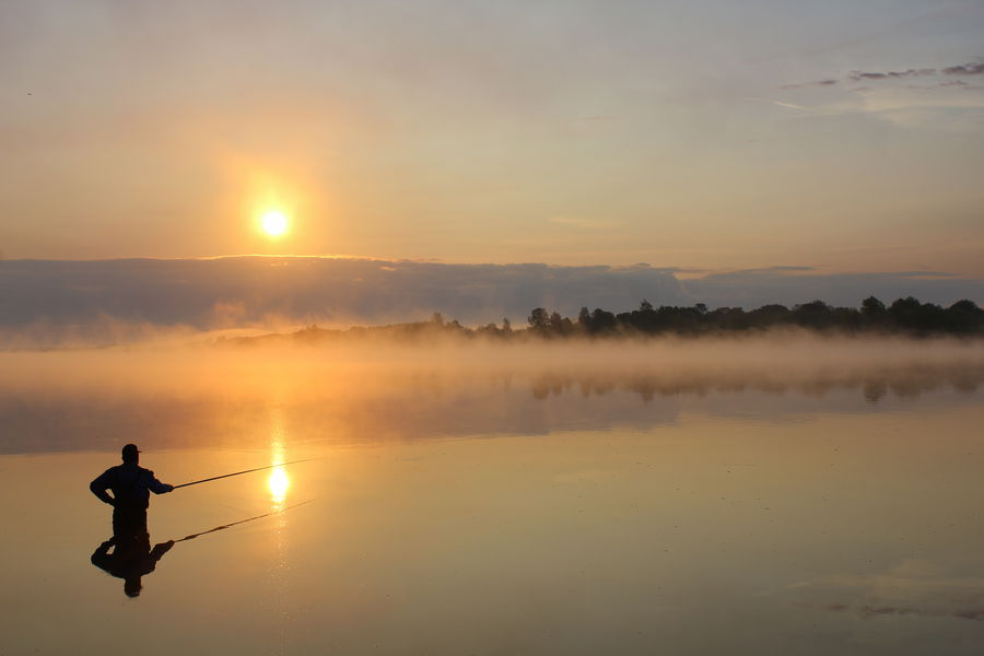 Angler fishing from shore on calm water during early morning light